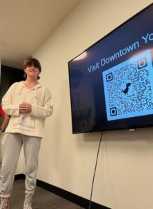 Student standing to the left of a television screen with a QR Code for Downtown York on it