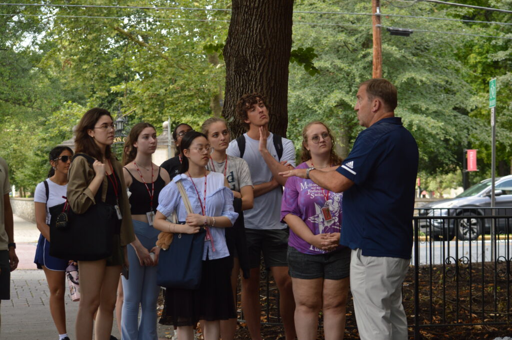 Students standing outside listening to a man talk