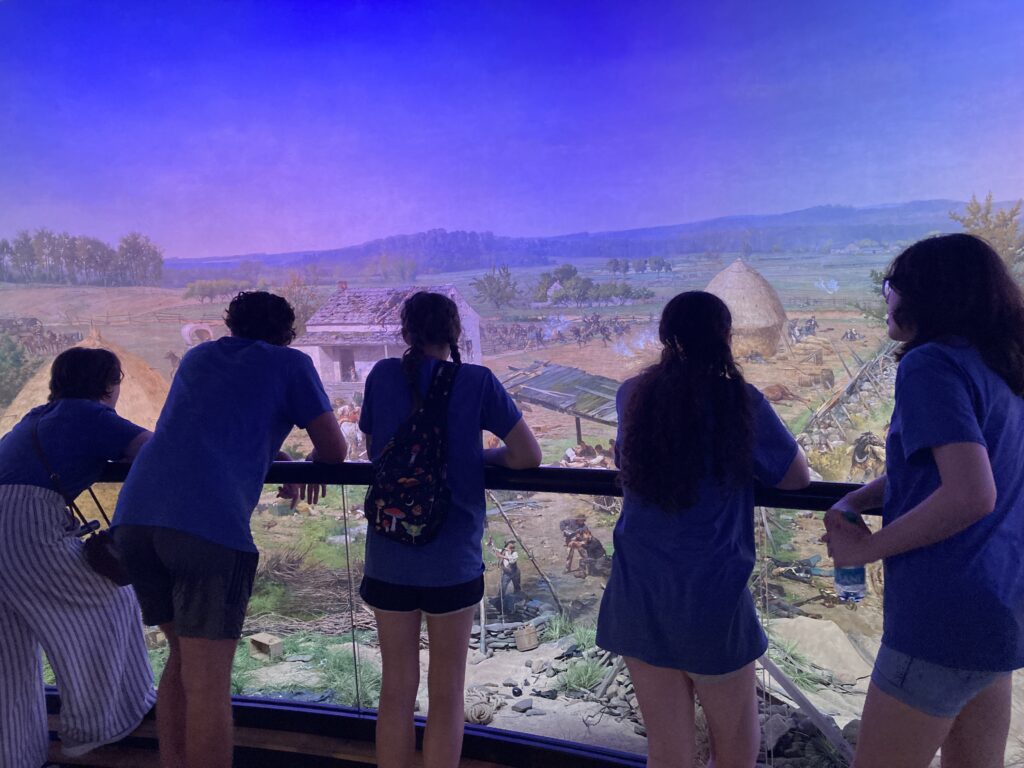 Students standing in front of a large painting of a battle
