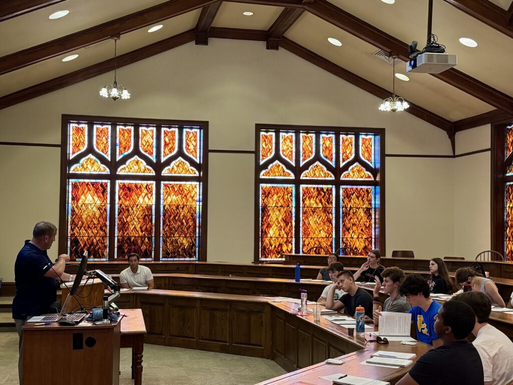A group of students sitting in a room with orange stained glass windows