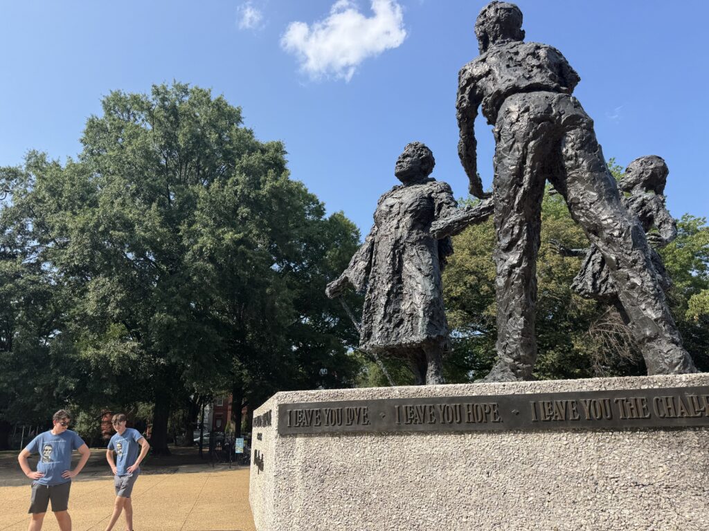 Two boys standing in front of a statue of three figures