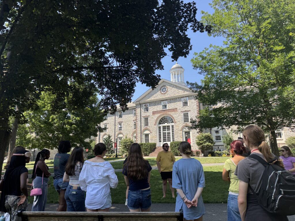 A large group of students standing outside of a light grey building.