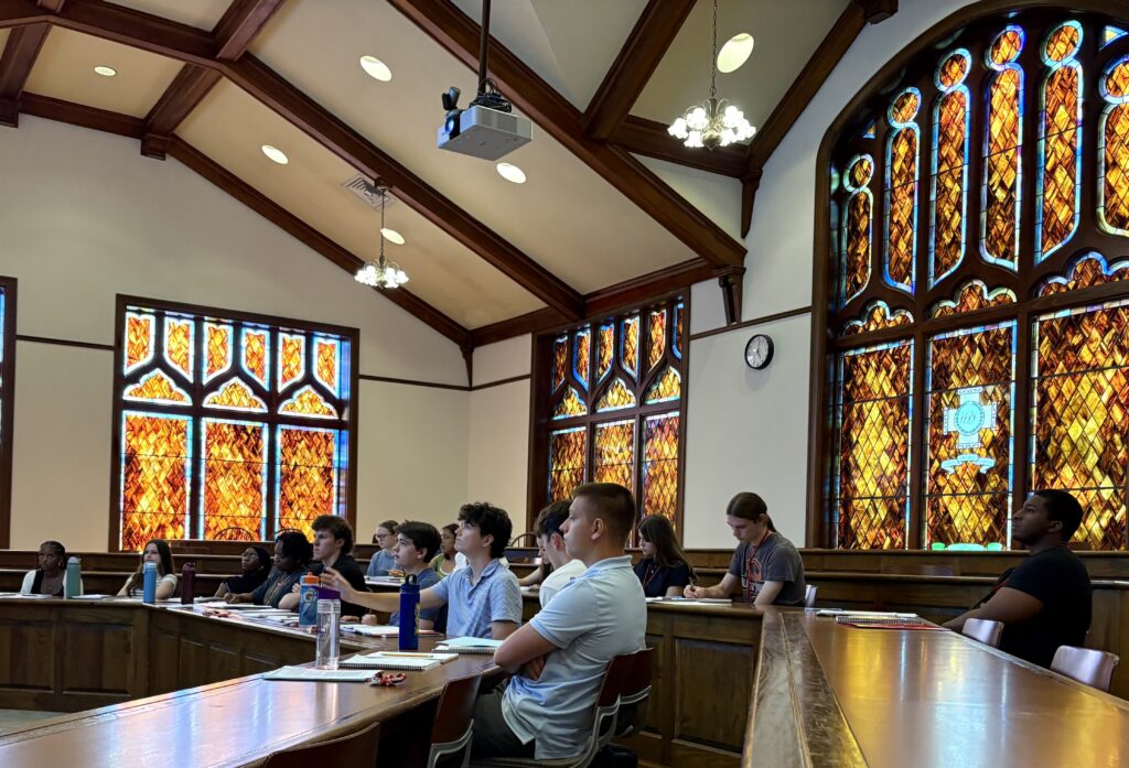 Students sitting in a classroom with orange stained glass windows.