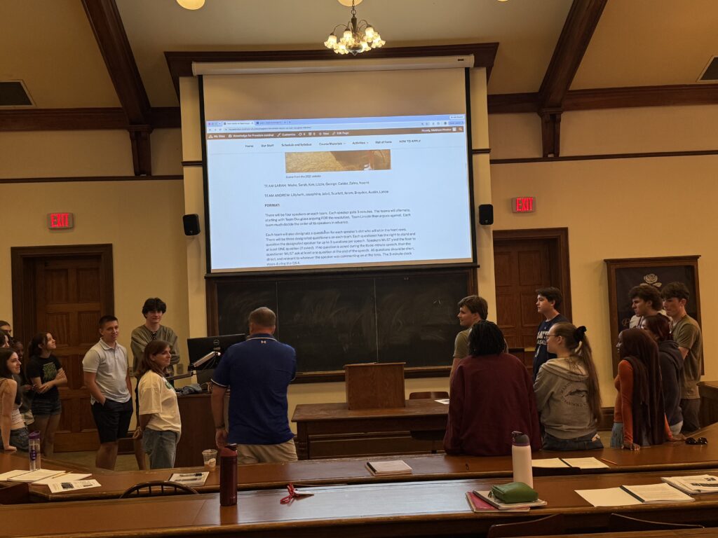 Two groups of students standing on either side of a chalkboard 