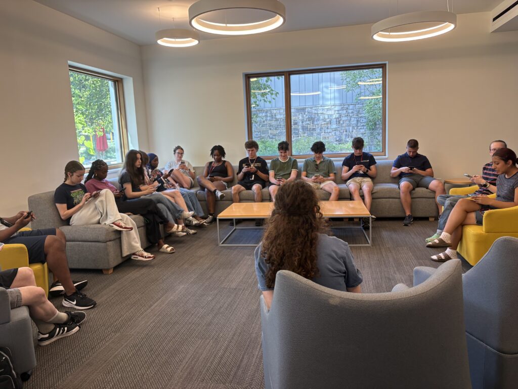 A group of students sitting on a couch, looking at their phones, and sharing their phone numbers with one another