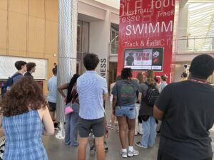 Students learning about the fitness center while standing in front of a display console