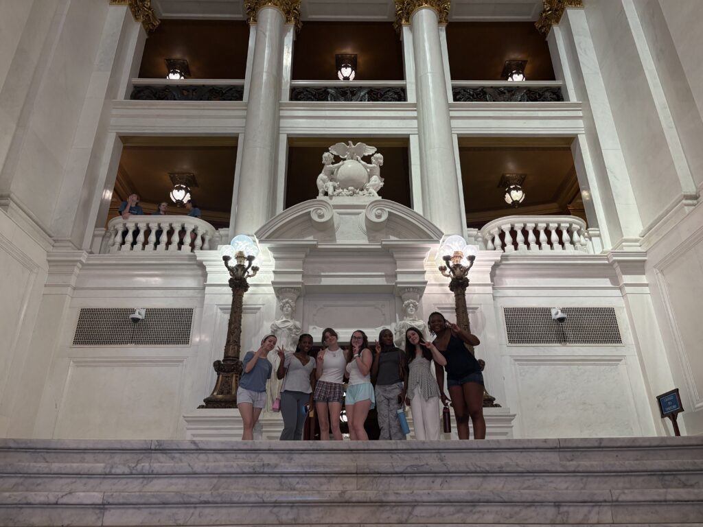Seven girls holding peace signs on top of a flight of stairs in the beautiful capital rotunda