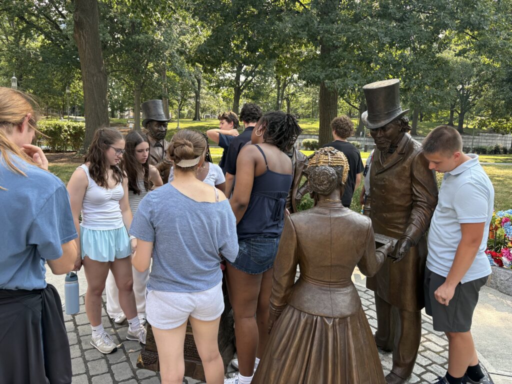 Students reading, touching, and observing the four statues of the monument
