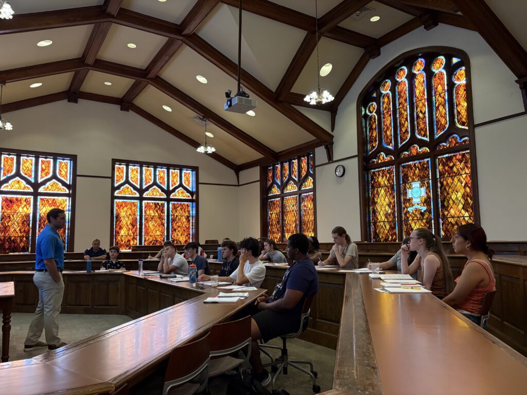 Professor Mealy standing in front of the students, giving a lecture on American feminism in Denny 317, stained glass in the background