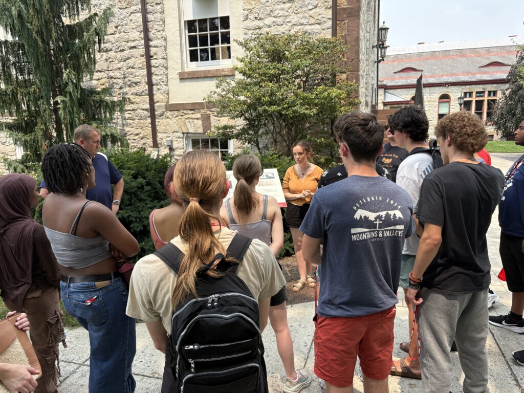Students standing in a semicircle, listening to Sarah speak about Dickinson's legacy regarding slavery