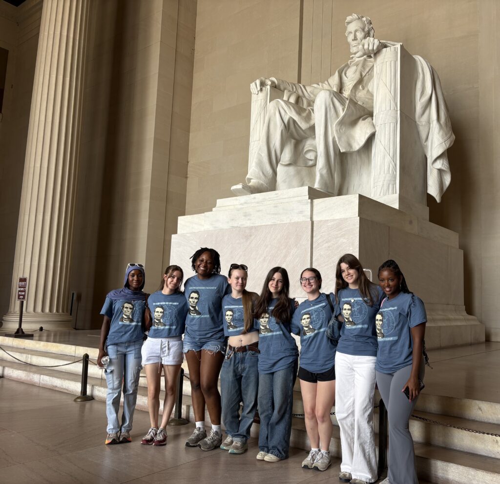 A group of girls standing in front of a large marble statue of a seated man