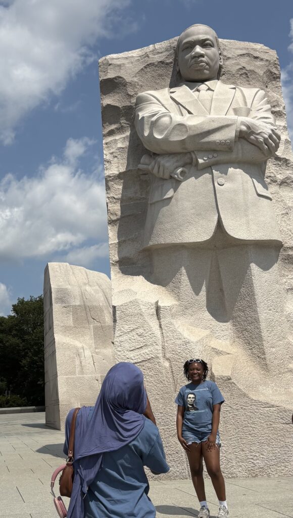 A girl taking a photo of another girl in front of a marble statue of Martin Luther King Jr.
