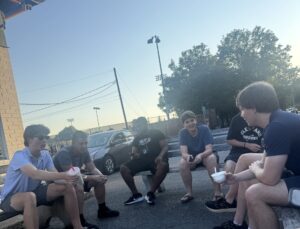 Students and staff sitting on benches talking with each other while eating ice cream and drinking milkshakes