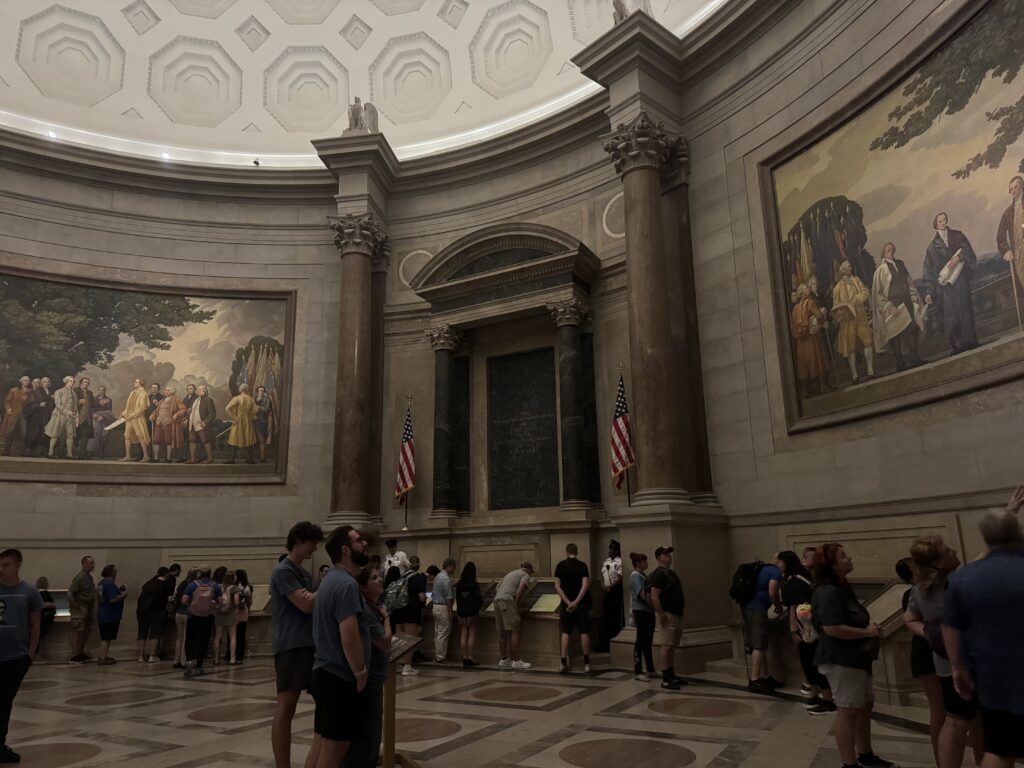 Students and staff observing the paintings in the rotunda of the National Archives building