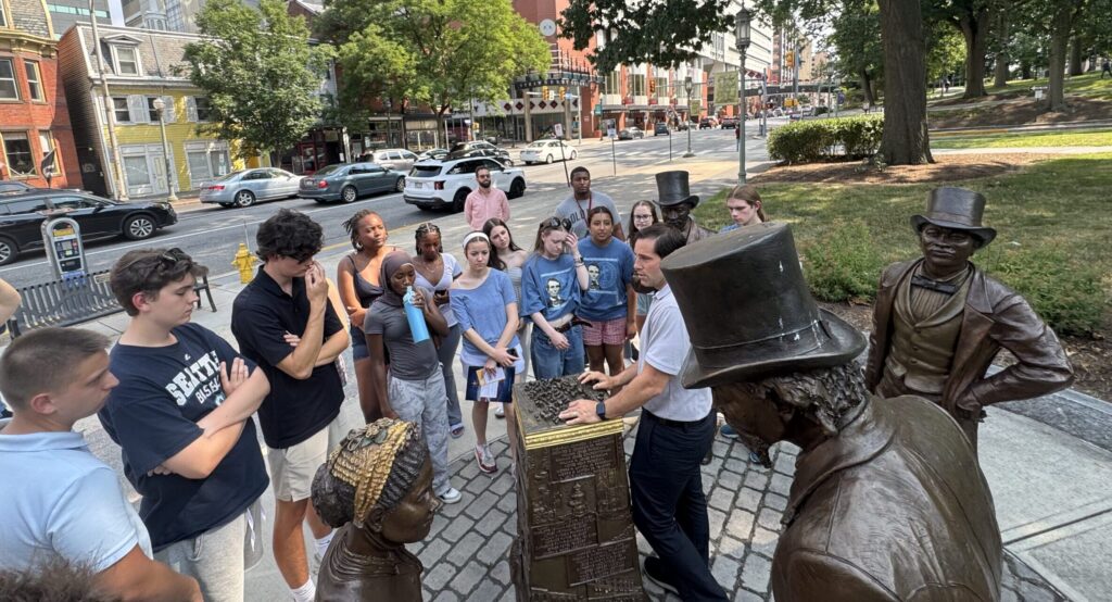 A group of students standing at a monument with four statues