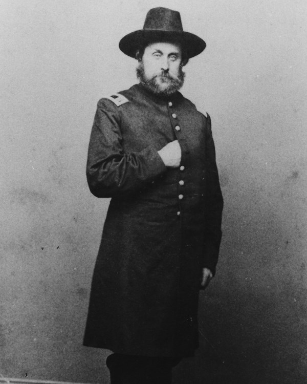 Capt. Theron E. Hall in military uniform, wearing a broad-brimmed hat and standing, posed with his right arm folded over his chest and partially concealed in his uniform. 