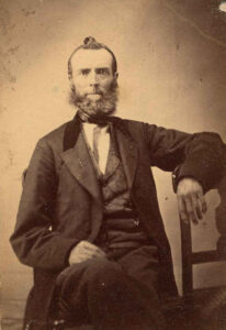man, with beard, seated, arm over chair